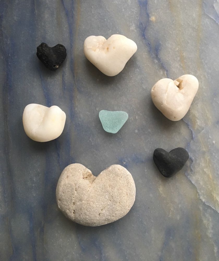 Six stone hearts and one glass one, on a background of sky-blue stone.