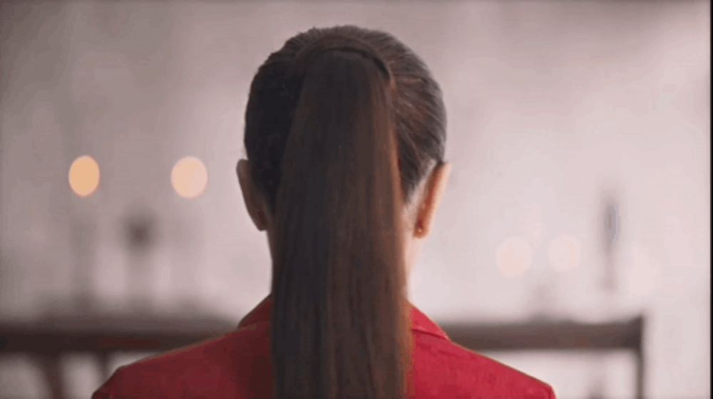 a woman wearing a red jacket and a ponytail is standing in front of a table .