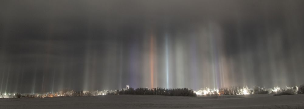 light pillars of white, green, purple, blue, red and orange tower over a snowy field