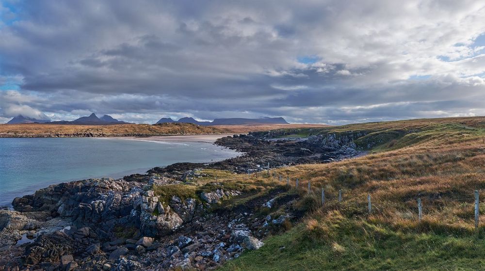 Landscape image of a beach with hills beyond and a bright but cloudy sky.