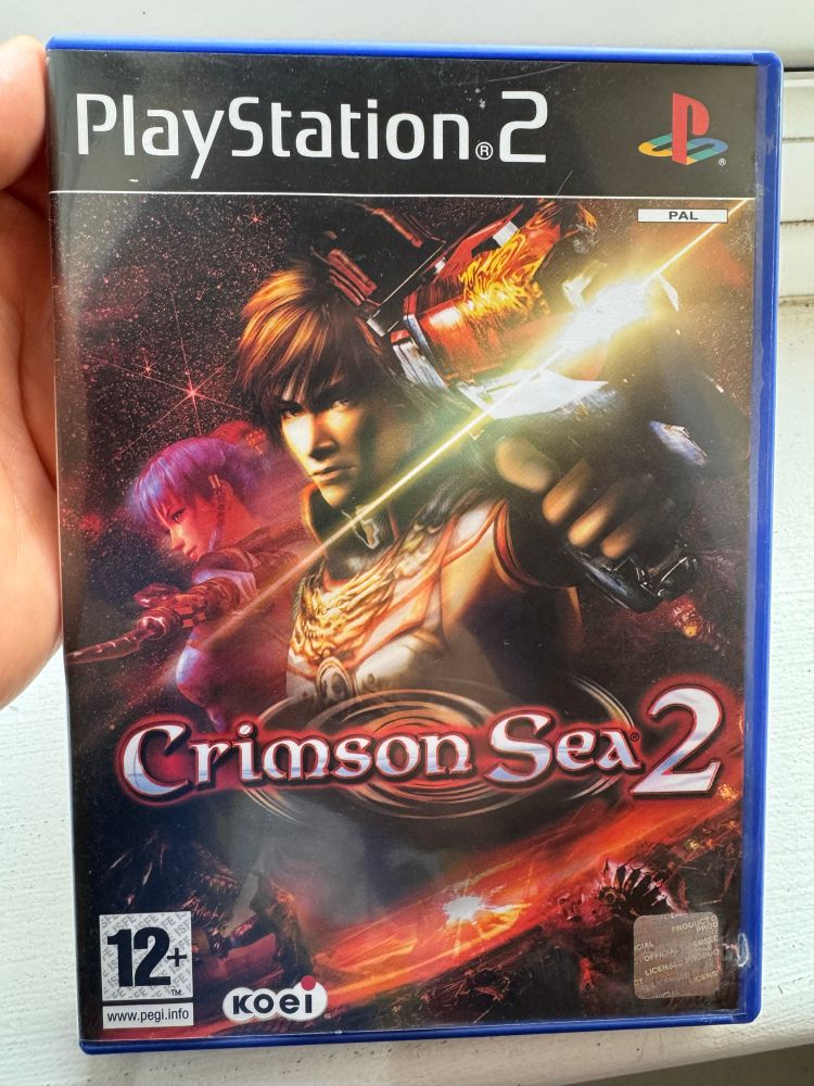 The box for Crimson Sea 2 for PlayStation 2, featuring the two lead characters in close-up: a young male action-hero type in armour, wielding a space pistol, and a female anime-girl with purple hair holding a blade.