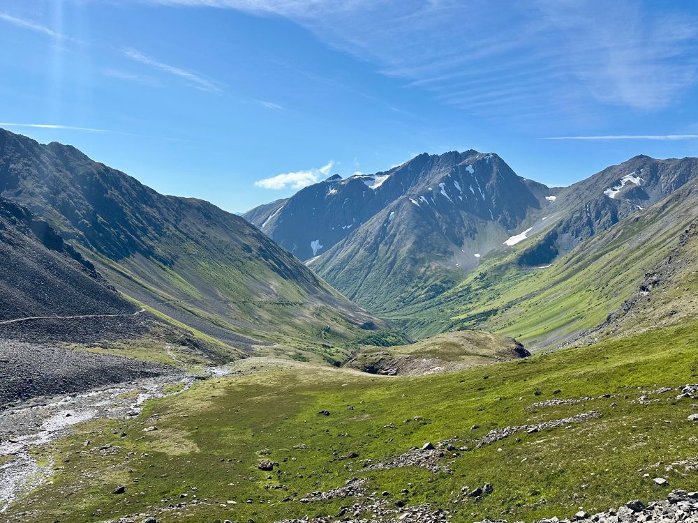 A green glacial valley with a trail cutting through the scree along the side. 