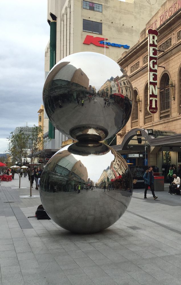A pair of proud mirrored spherical sculptured balls standing stacked together in an outdoor Adelaide shopping mall. 