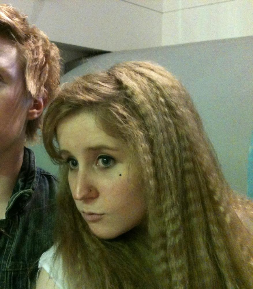 Photo of a white woman with blonde crimped hair. She is looking to the left of the camera and is pouting. 