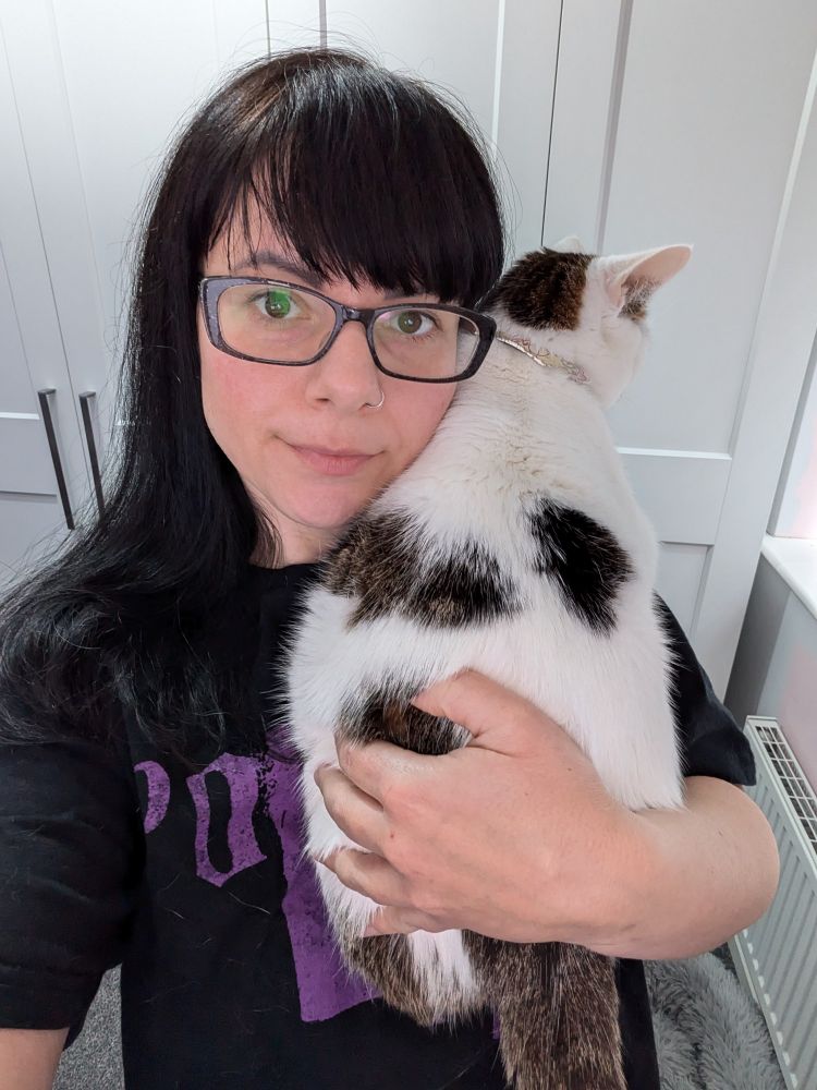 White cat with tabby patches is being cuddled by a woman in her left arm. The cat is partly over the woman's shoulder and is obviously very comfortable.