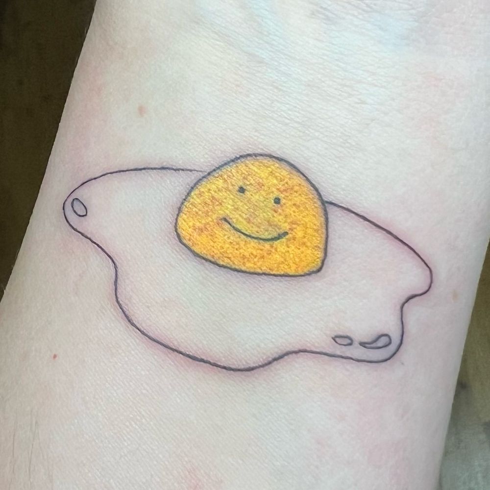 Tatuaje recién hecho en muñeca de un huevito frito sonriente