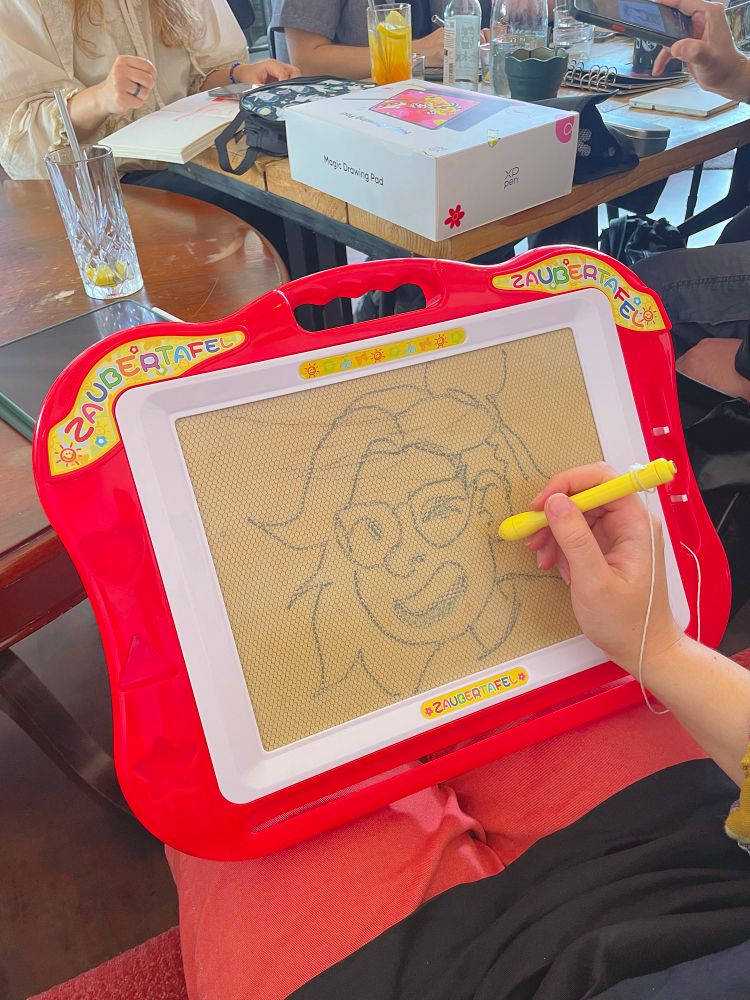 Picture of a retro magic drawing pad toy with a drawing in it. In the background is a packaging for a xp-pen digital magic drawing pad