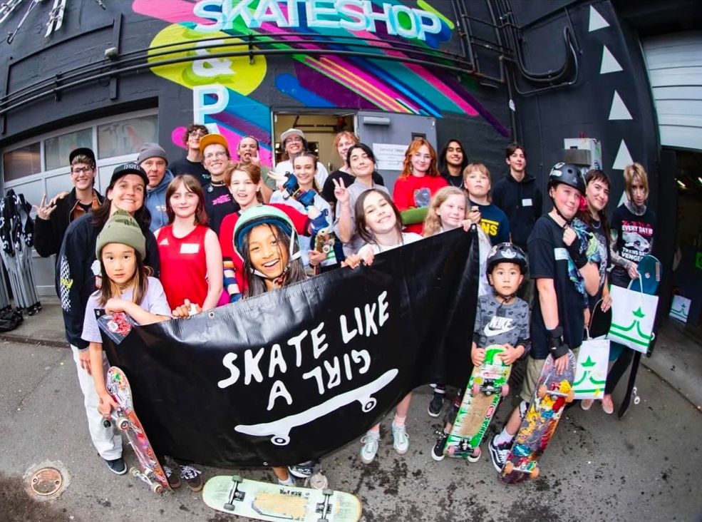 A crowd of skateboarders in a group picture with the front line holding a "skate like a girl" banner.