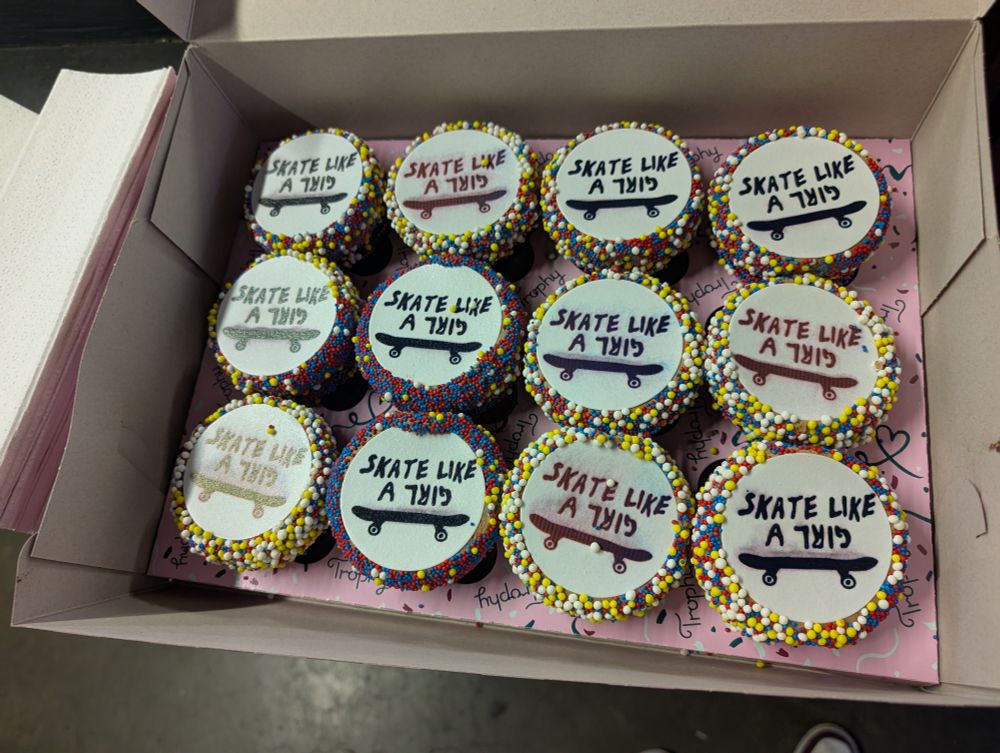 A box full of cupcakes featuring "skate like a girl" frosting with a skateboard on it.