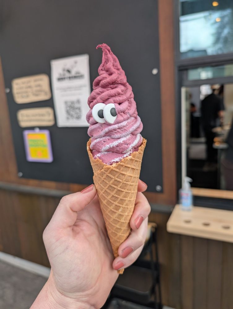 A lavender flavored ice cream on a cone with two candy eyes set in the middle of it.