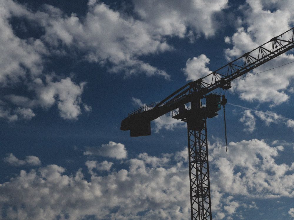 A picture of a construction crane against a cloudy sky, edited with warmer tones and a grain effect.