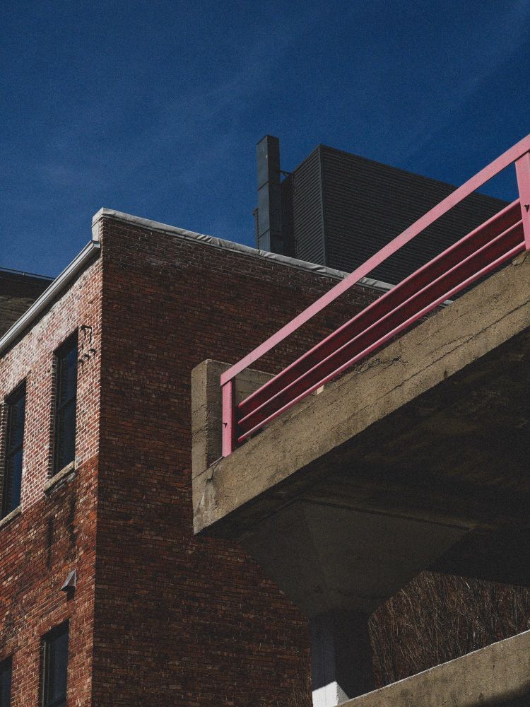 A photo with an up angle view of the corner of a parking garage in front of other various buildings and a blue sky, edited with warmer tones and a grain effect.