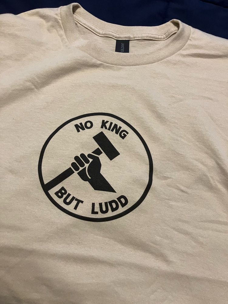 A tshirt with a logo showing a hand holding a sledgehammer that says “No king but Ludd”