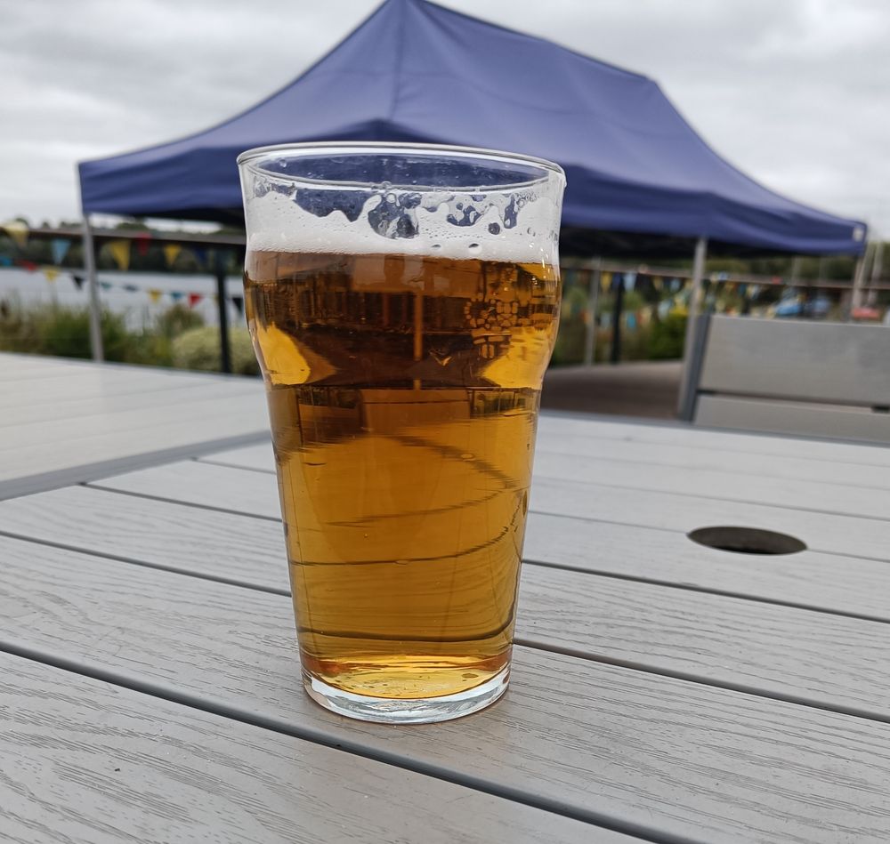 A blonde and refreshing pint sits atop a table with a blue pop up gazebo in the background.