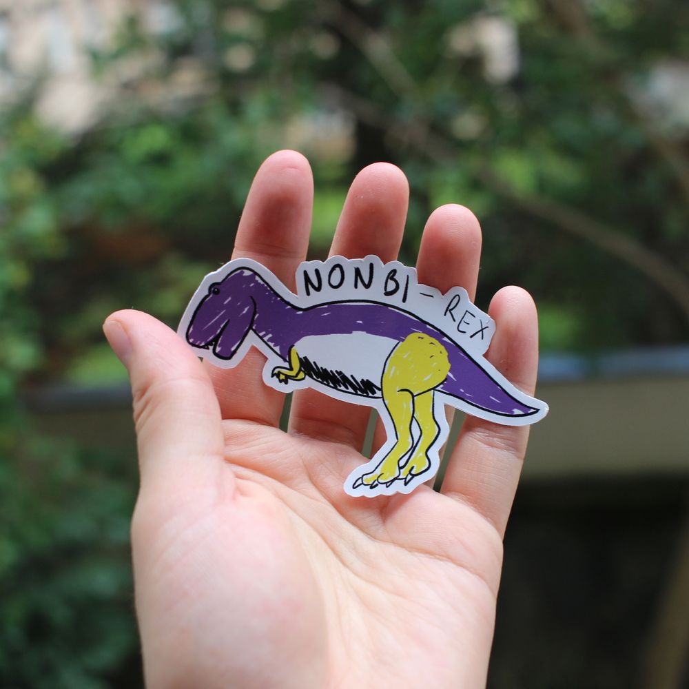 Photo d’un sticker. C’est un dessin de dinosaure au crayon, avec un effet un peu mal colorié. Il représente un T-rex aux couleurs non-binaires, avec écrit « Non Bi-rex » au-dessus. Le mot « Non Bi » est en gras.