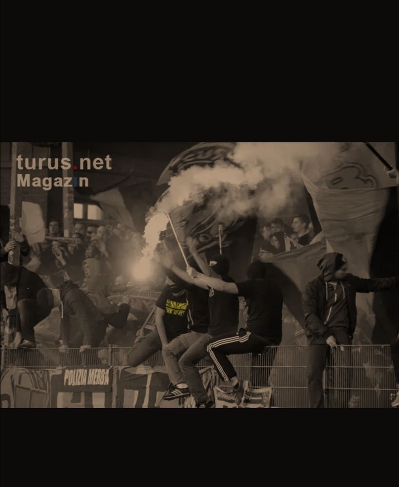 Fußballfans, teilweise vermummt, mit Pyrotechnik in der Hand aufm Zaun im Stadion. 