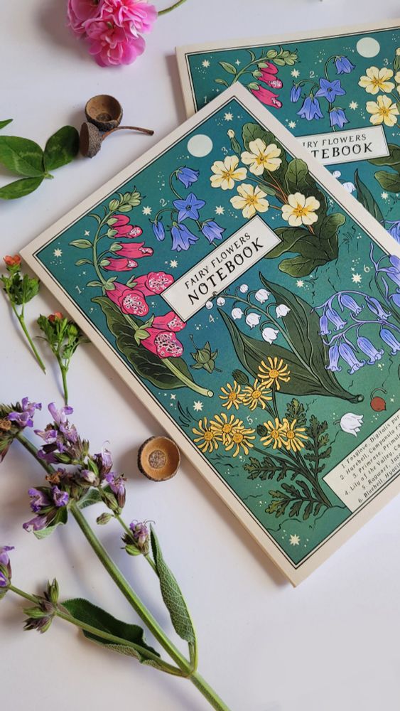 brightly illustrated notebooks with botanical artwork with a teal background. it features foxglove, harebell, primrose, lily of the valley, ragwort and bluebell. in the middle is the title fairy flowers notebook. these are flowers associated with the fae in folklore. on the back of the notebook are snippets of the fairy folklore and the plants uses.