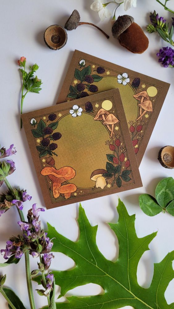 two autumnal notepads surround by plants - leaves, flowers and acorns on a white background. the notepads themselves are illustrated with an autumnal themed frame, featuring the fairy ring mushroom, rose hip, weeping bolete, saffron milk cap, and acorn and blackberry. these are all edible plants that can be found in Australia and are also invasive/not native.