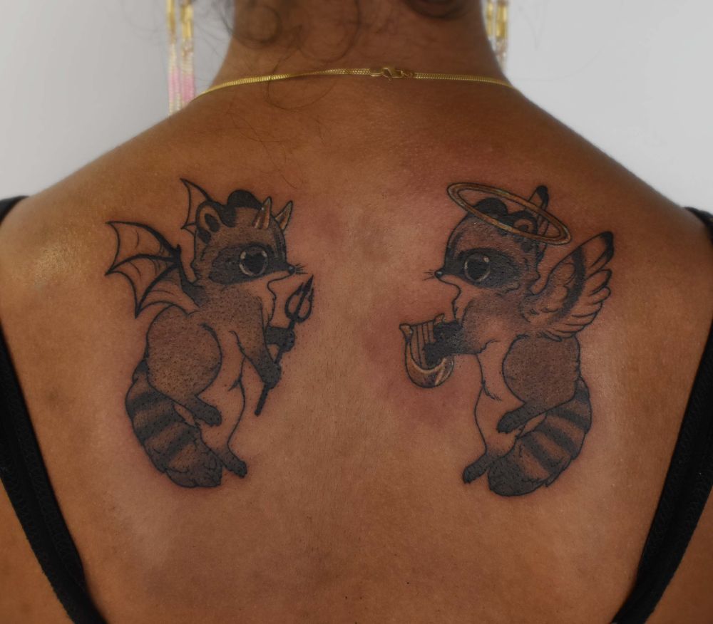 two symmetrical tattoos on the shoulder blades of an angel and devil racoon