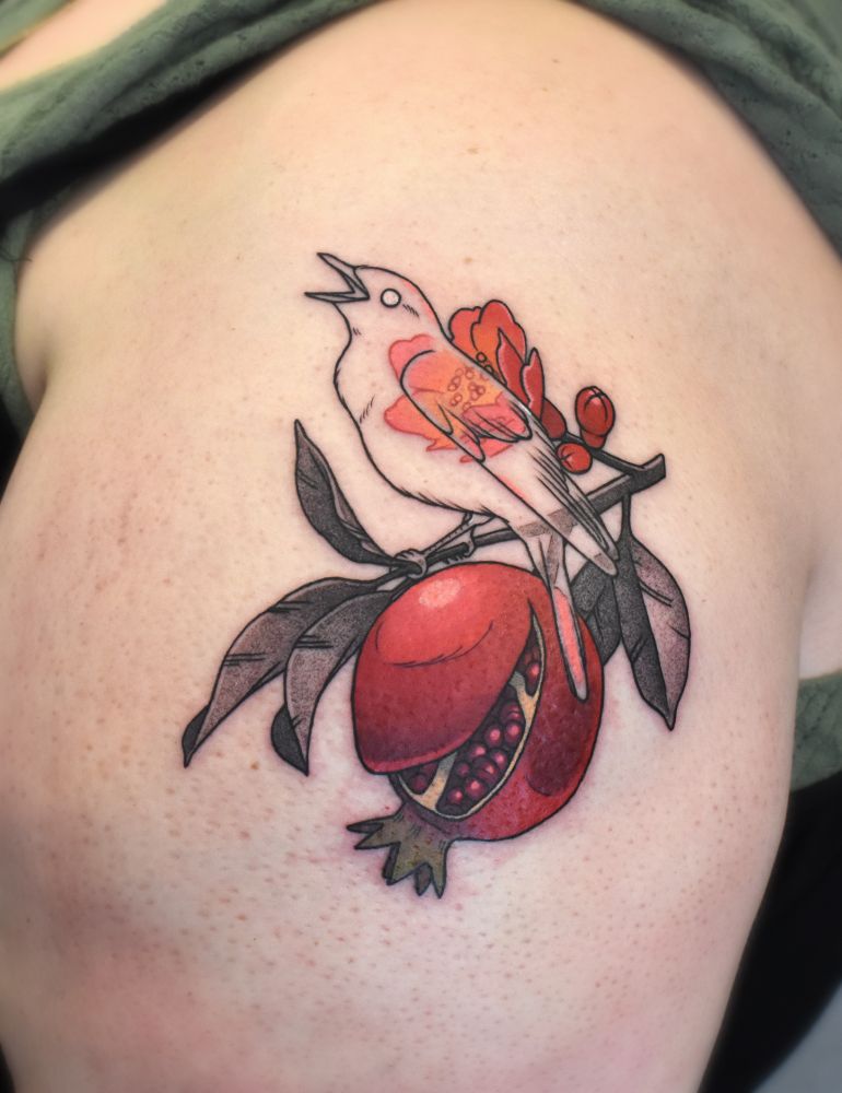 a tattoo of a pomegranate branch with a split pomegranate, and a ghostly nightingale sitting on the branch in front of a flower which shows through it's transparent body