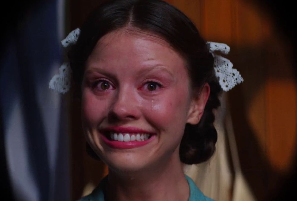 Mia goth in the movie Pearl, smiling and crying 