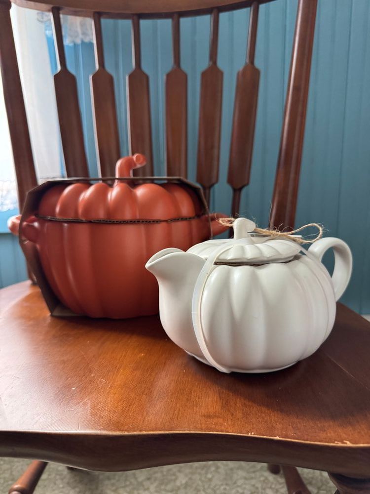 A white gravy boat in the shape of a pumpkin (right) and an orange pumpkin casserole dish sit on a wood chair against a blue wall.