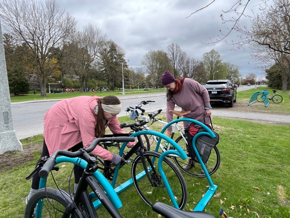 Persons unlocking their bikes from blue bike racks shaped like sets of waves
