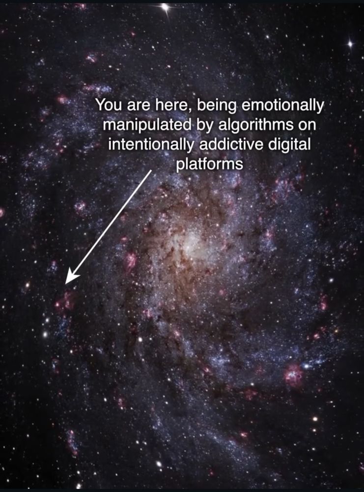 the sparkling spiraling universe littered with scattered glimmering galaxies with an arrow pointing to one. text reads “You are here, being emotionally manipulated by algorithms on intentionally addictive digital platforms”