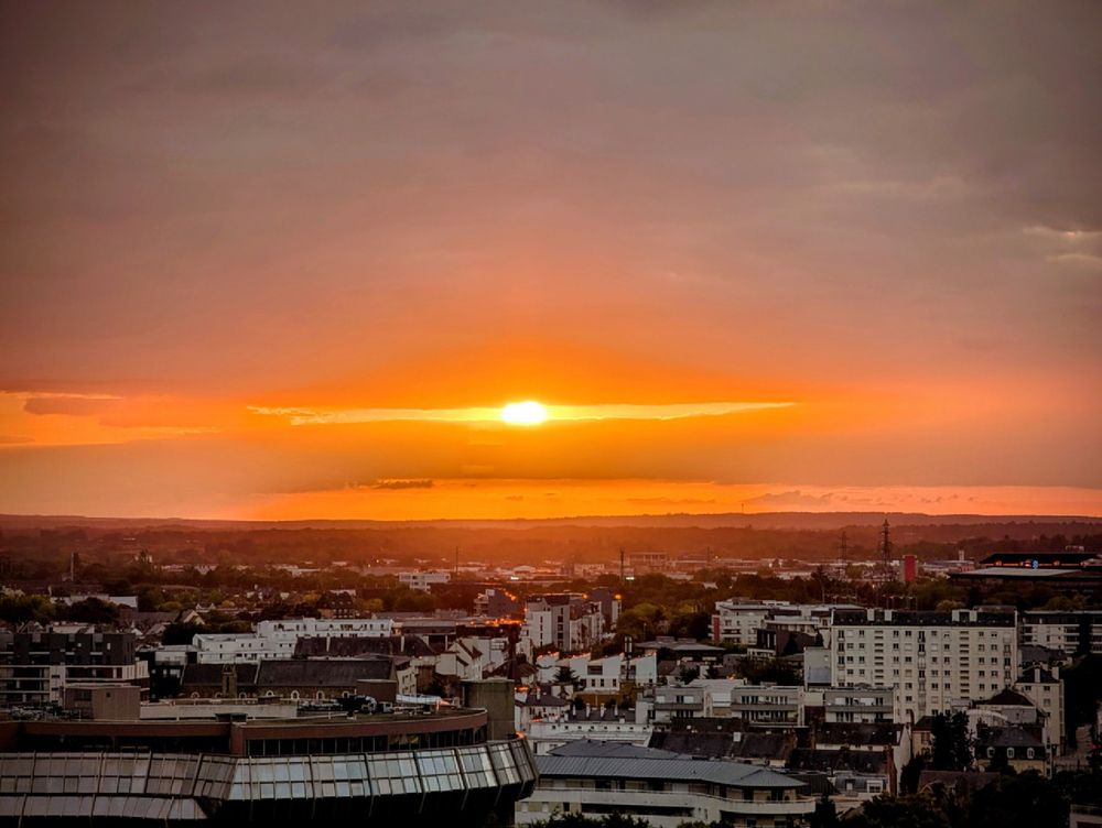 Coucher de soleil qui émerge juste d'un ciel très chargé et nuageux en plein coeur de ville depuis un immeuble dans les étages supérieurs. Encore plus zoomé sur le soleil. 