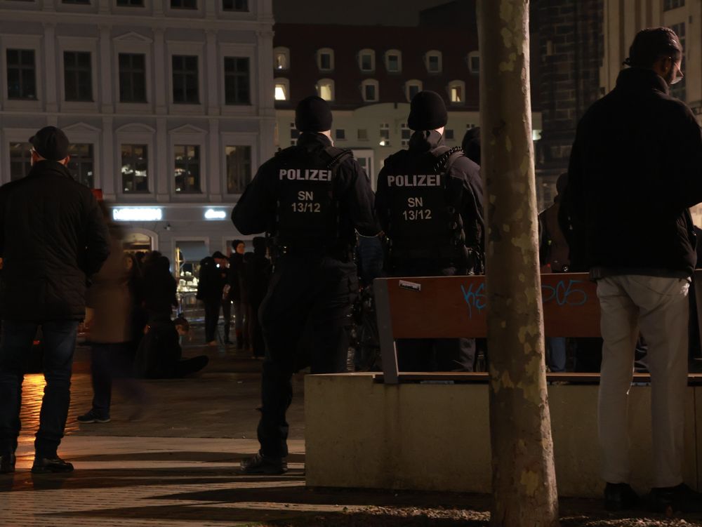 Zwei Polizisten stehen zur Absicherung einer Demonstration vor einer Bank. Auf den Rückennummern steht 13/12. 