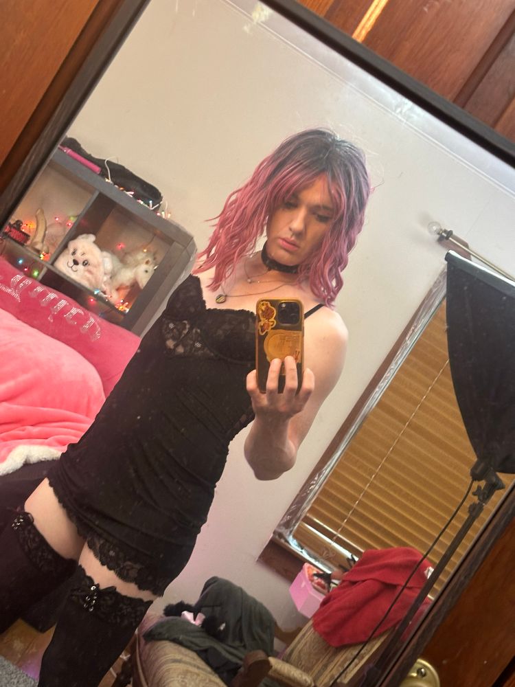 Lilly taking a mirror selfie wearing a little black dress with black thigh highs 