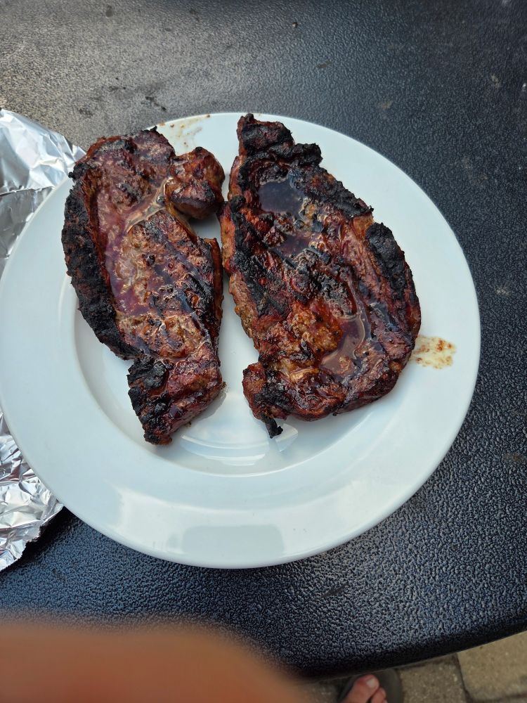 Two grilled ribeye steaks on a white plate resting after the cook