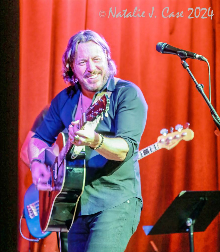 Steve Carlson on stage at the Hotel Cafe, red curtain backdrop, guitar