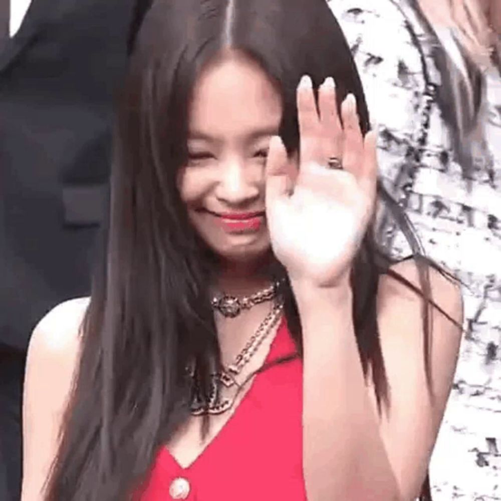 a woman in a red dress is waving at the camera while wearing a ring on her finger .