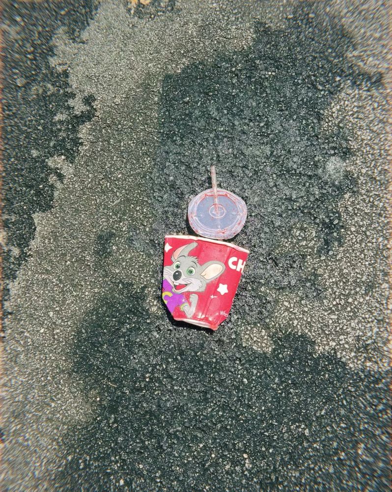 A smushed “chuck e. cheese” disposable drink cup on the pavement. 