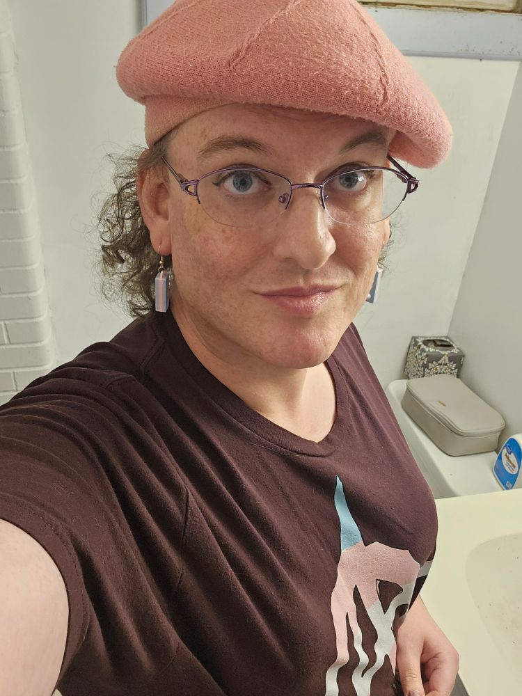 Cesena, wearing a pink beret and a brown tee with an anarchy symbol colored in tabs pride shades