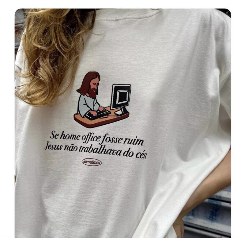 camiseta branca com um desenho de jesus em uma mesa marrom digitando em um teclado e olhando uma tela de computador. embaixo do desenho tem os dizeres: 
Se home office fosse ruim 
Jesus não trabalhava do céu
possui uma logo da marca Sometimes