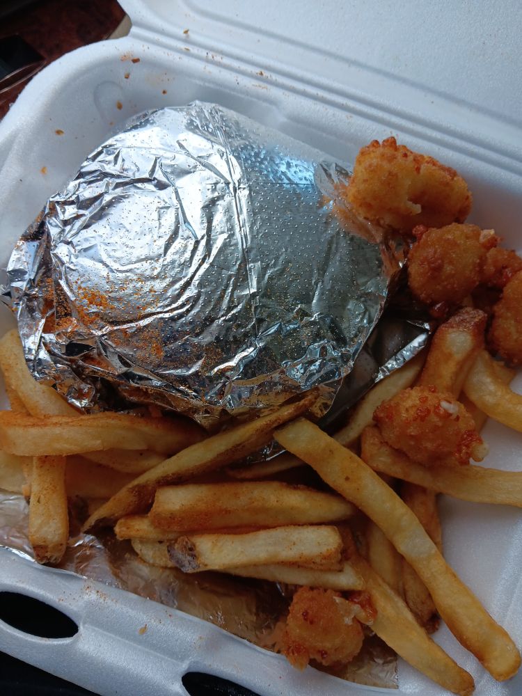 A burger wrapped in foil, several cheese bites, and cajun fries. All in a styrofoam tray.