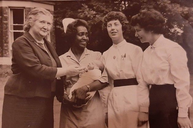 Daphne Steele holding a child, with other women from healthcare