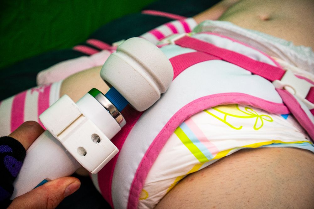 Caucasian male, laying on bed. Bound by a segufix clone in white with pink colours, that he made himself. Thickly diapered being buzzed by a magic wand