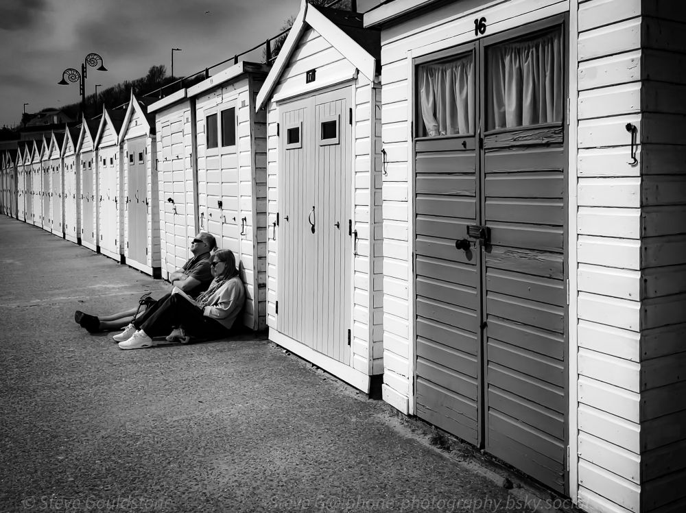 A couple resting in the spring sunshine, Beach huts, Lyme Regis, Dorset, England.  