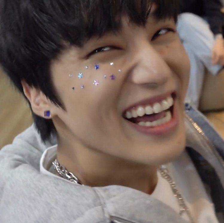 Jung Wooyoung (ATEEZ) laughing/smiling with sparkly star stickers on his cheeks and ears.
