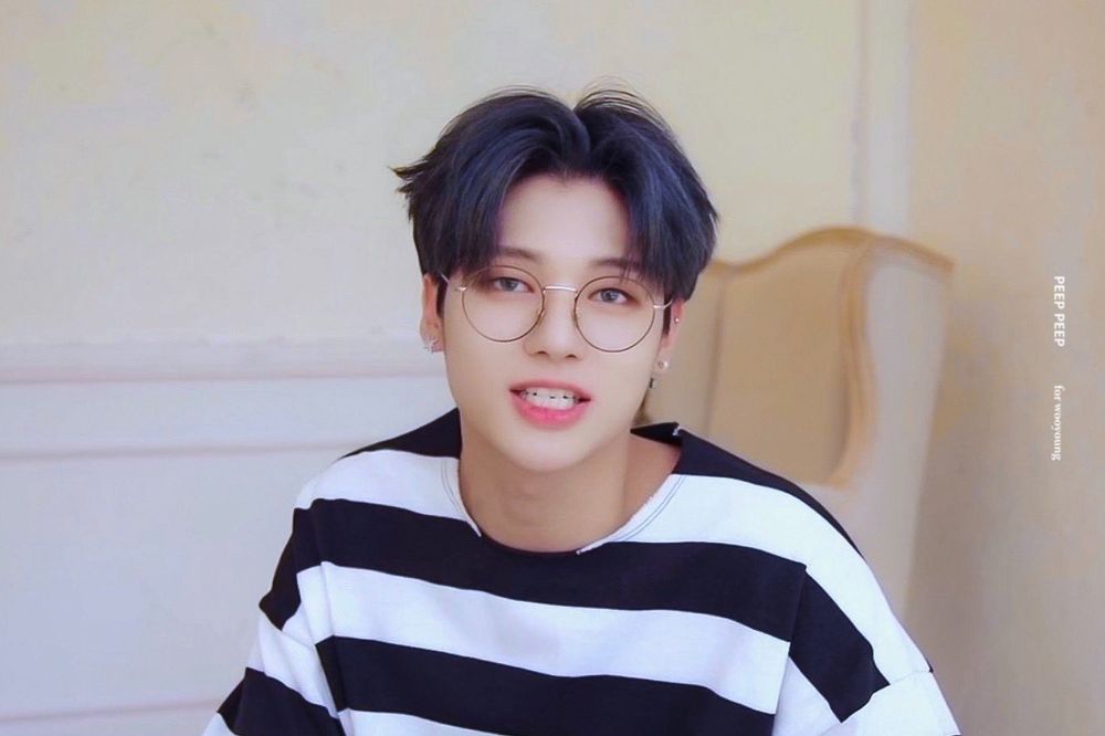 Jung Wooyoung of ATEEZ smiling at camera wearing glasses and a striped shirt, caption credits image to (peep peep for wooyoung)