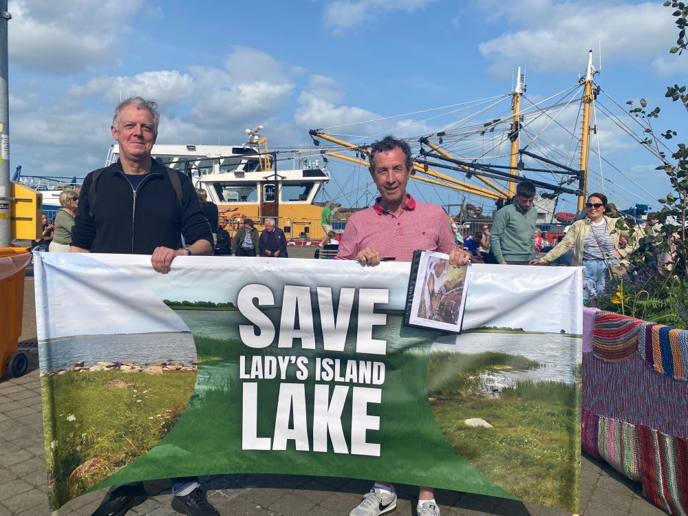 A picture of two volunteers holding the Save Lady's Island Lake banner on Wexford Quay during Fleadh Cheoil na h-Éireann.