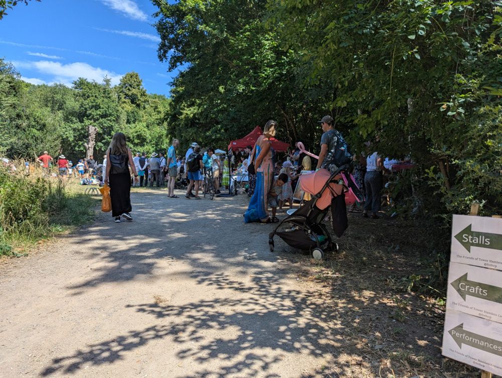 A long shot of the fair, most people under the shade of tall trees