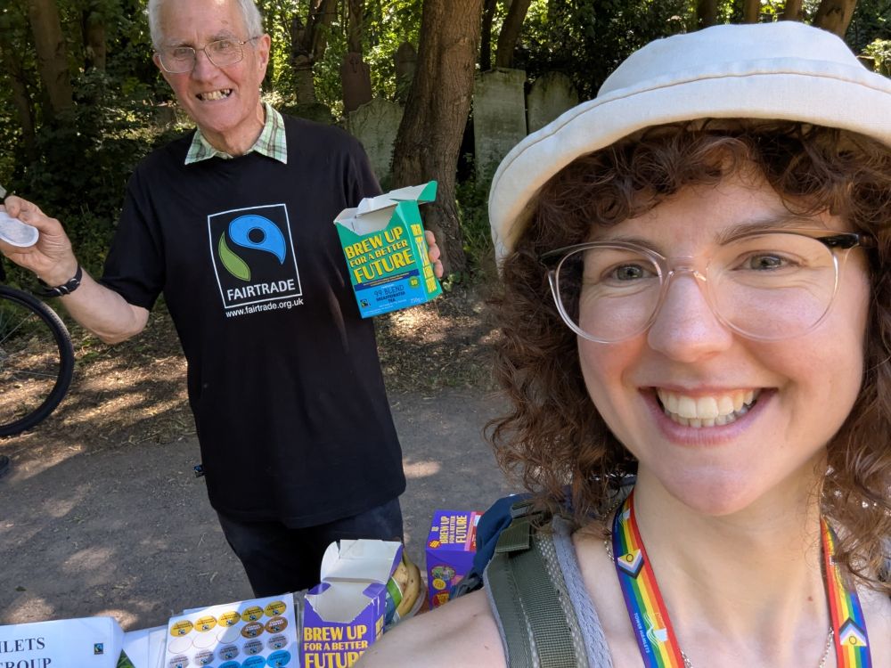 A selfie of Nathalie with Owen Beith - fair trade campaigner holding fair trade tea with a stand full of resources and information about fair trade