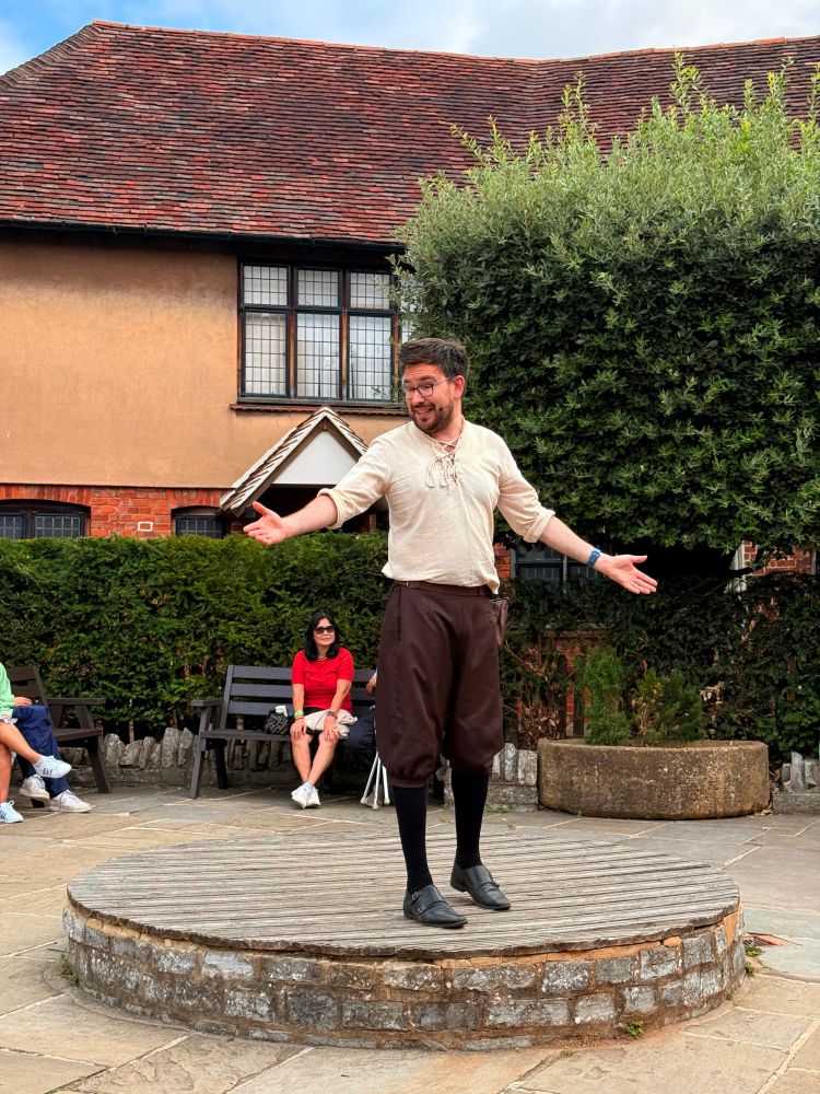 En mann i enkelt teaterkostyme fremfører Shakespeare på en liten plattform utendørs. 