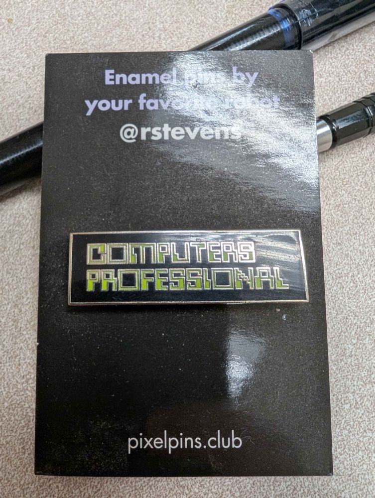 It's the card carrying an enamel pin that reads COMPUTERS PROFESSOINAL in a green-on-black pixely "computers are the future" sort of font. The backing card reads Enamel pins by your favorite robot @rstevens, pixelpins.club, and of course the pin is in the middle.