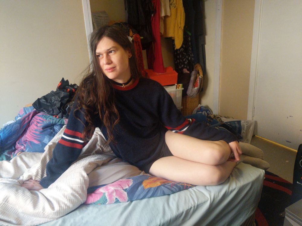 me, on the bed, gazing wistfully out the window, in a cute mostly-black jumper, red and white stripes at the elbows