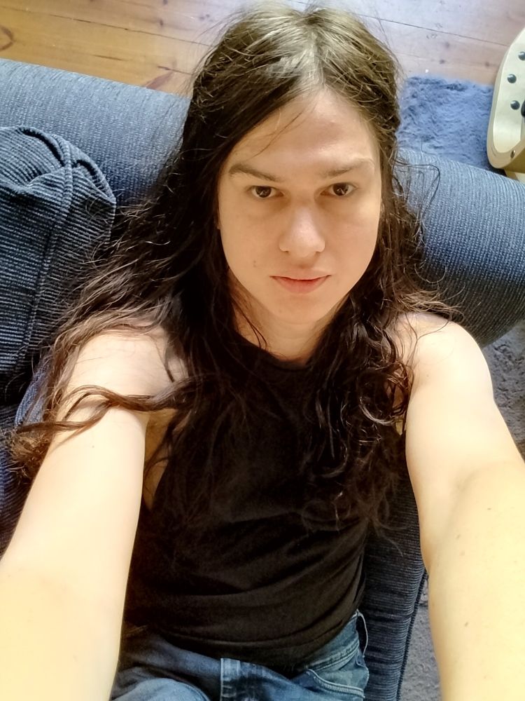 im sitting on a couch in a black tank top sorry it's difficult to explain how im so pretty in this one but i am, kinda white boyband jesus